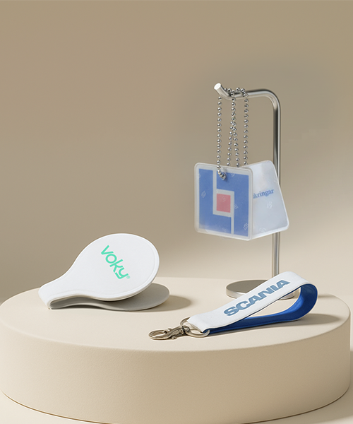 Närbild av tre reflexprodukter: en vit klämreflex (Voky), en hängande fyrkantig reflex och en nyckelring (Scania).