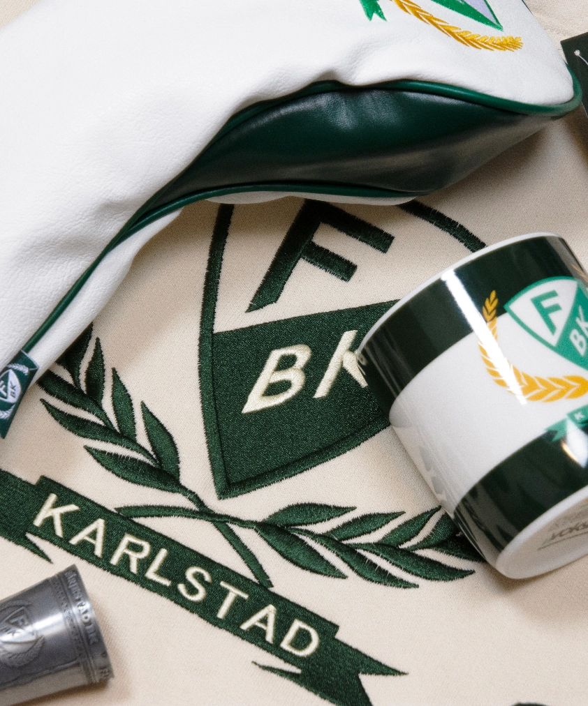 En närbild på Färjestad BK merchandise: ett beigefärgat tyg med broderat klubbmärke och "KARLSTAD", ett golfklubbsfodral och en mugg