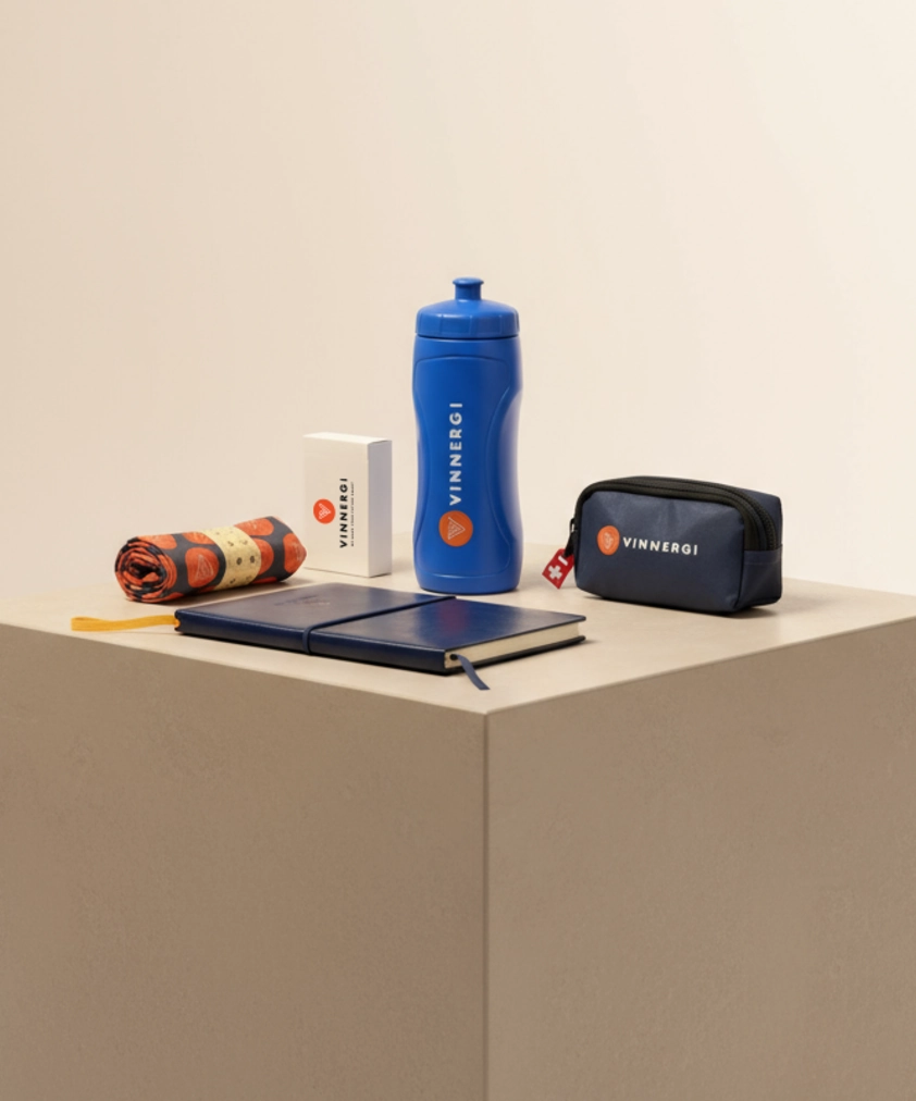 En samling Vinnergi-märkta föremål: en blå vattenflaska, en blå anteckningsbok, en liten marinblå påse och en ihoprullad handduk.